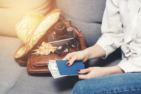 Woman holding passport and dollars cash currency, packing leather backpack with retro camera, straw hat, sunglasses. Concept of traveling and vacations.の写真素材