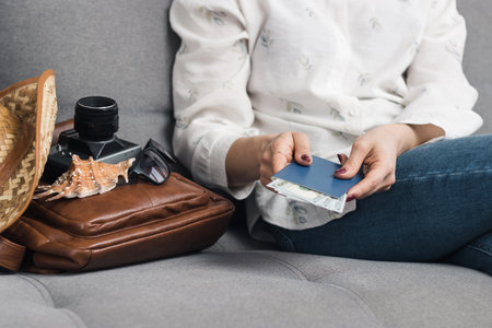 Woman holding passport and dollars cash currency, packing leather backpack with retro camera, straw...
