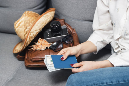 Woman holding passport and dollars cash currency, packing leather backpack with retro camera, straw hat, sunglasses. Concept of traveling and vacations.の写真素材