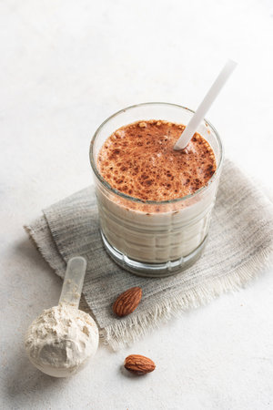 Glass with protein drink, healthy milkshake smoothie on white table with protein powder in measuring spoon and almond nuts.の写真素材