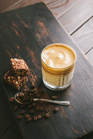 Dalgona coffee drink, cocktail with whipped instant coffee and milk in a glass on a wooden board with a healthy protein bar.の写真素材