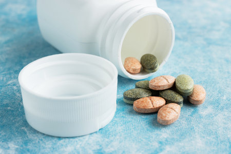 Multicolored medical pills, drugs or tablets for treatment on blue background, vitamins and...