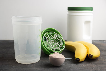 Whey protein powder with a chocolate flavor in a plastic measuring spoon on a dark background with...