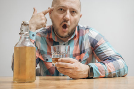 Addicted and drunk man at the table with a glass of alcohol drink, whiskey or brandy, alcoholism and bad habits concept.の写真素材