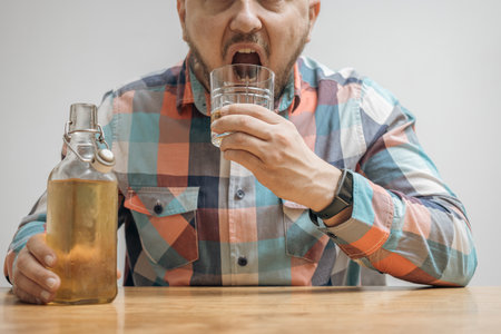 Addicted and drunk man at the table with a glass of alcohol drink, whiskey or brandy, alcoholism and bad habits concept.の写真素材