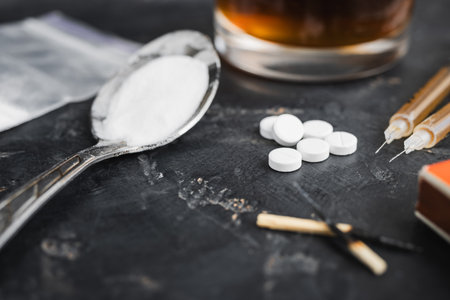 Narcotic substances in spoon, dope powder in transparent plastic bag, syringes with drugs dose, white pills and glass of alcohol drink on textured background. Concept of addiction and bad habits.の写真素材