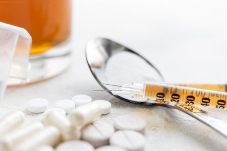 Narcotic substances in spoon, dope powder in transparent plastic bag, syringes with drugs dose, white pills and glass of alcohol drink on textured background. Concept of addiction and bad habits.の写真素材