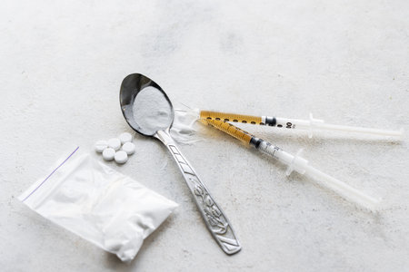Narcotic substances in a spoon, dope powder in transparent plastic bag, syringes with dose of drugs and white pills on a textured background. Concept of addiction and bad habits.の写真素材