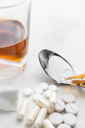 Narcotic substances in spoon, dope powder in transparent plastic bag, syringes with drugs dose, white pills and glass of alcohol drink on textured background. Concept of addiction and bad habits.の写真素材