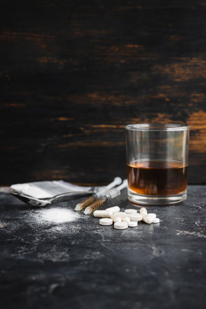 Narcotic substances in spoon, dope powder in transparent plastic bag, syringes with drugs dose, white pills and glass of alcohol drink on textured background. Concept of addiction and bad habits.の写真素材