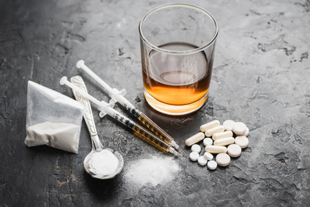 Narcotic substances in spoon, dope powder in transparent plastic bag, syringes with drugs dose, white pills and glass of alcohol drink on textured background. Concept of addiction and bad habits.の写真素材