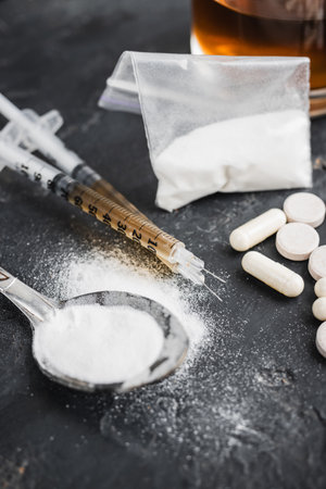 Narcotic substances in spoon, dope powder in transparent plastic bag, syringes with drugs dose, white pills and glass of alcohol drink on textured background. Concept of addiction and bad habits.の写真素材