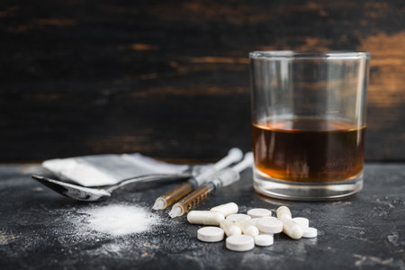Narcotic substances in spoon, dope powder in transparent plastic bag, syringes with drugs dose, white pills and glass of alcohol drink on textured background. Concept of addiction and bad habits.の写真素材