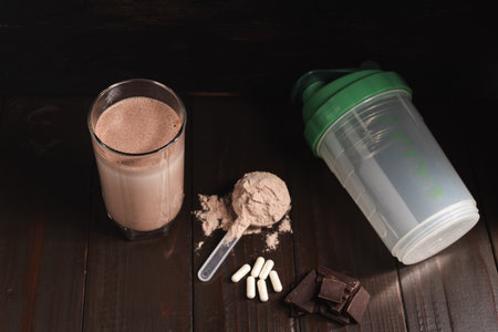 Protein milkshake cocktail in a glass, plastic measuring spoon with whey protein powder, white pills...