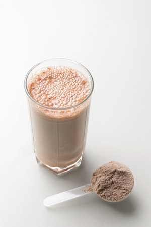 Protein drink cocktail in a glass and whey protein powder in a measuring scoop.の写真素材