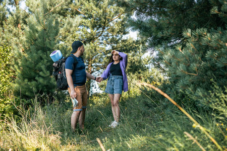 Couple tourists with backpacks walking outdoors in the summer forest, tired and emotional woman.