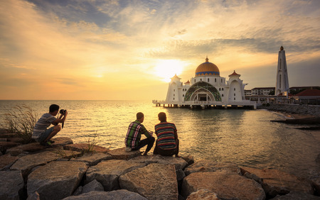 Three traveler with beautiful sunset  - at Malacca Straits Mosque ( Masjid Selat Melaka). It is a mosque located on the man-made Malacca Island near Malacca Town, Malaysia.の写真素材