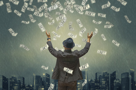 Back view of business man hug money with green tones dramatic rain & city background. Concept for success business. Motion blur money.の写真素材