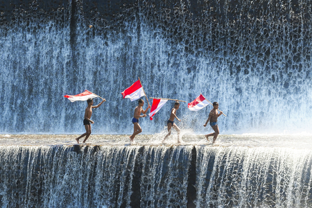 BALI - May 22 : Boys having fun and waving indonesian flag by playing water in an artificial dam on the Tukad Unda dam, Bali, Indonesia on May 22, 2014.のeditorial素材