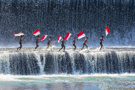 BALI - May 22 : Boys having fun and waving indonesian flag by playing water in an artificial dam on the Tukad Unda dam, Bali, Indonesia on May 22, 2014.のeditorial素材