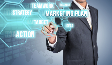 Businessman touching MARKETING PLAN concept. Businessman hand with virtual graphic and projections over blue backgroundの写真素材