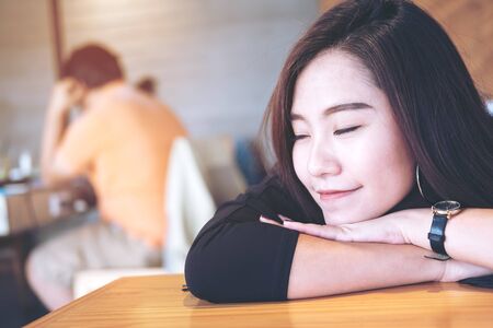 A beautiful asian woman sit with chin resting on her hands and closing her eyes in wooden cafeの写真素材