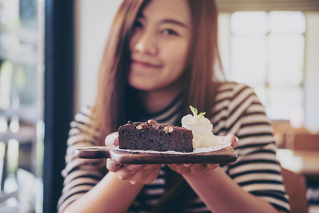 A beautiful asian woman holding brownie cake and whipped cream with feeling happy and good lifestyle in the modern cafeの写真素材