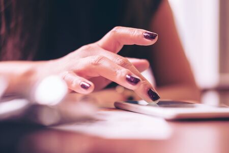 A business woman's hand touching and sliding finger on smart phone in modern cafeの写真素材