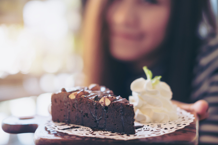 A beautiful asian woman holding brownie cake and whipped cream with feeling happy and good lifestyle in the modern cafeの写真素材