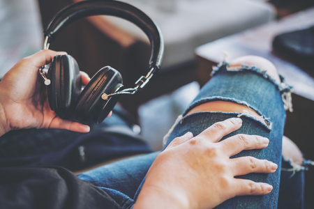 A woman wearing ripped jean , holding headphone and sitting in modern cafe with feeling relaxの写真素材