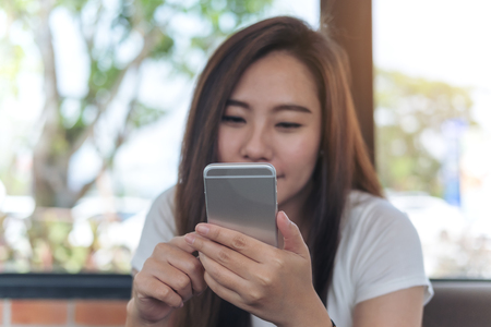 A  beautiful Asian girl with smiley face holding and using smart phone in coffee shopの写真素材