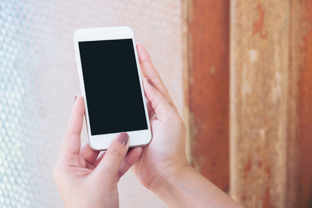 Mockup image of hand holding white mobile phone with blank black screen and vintage glass mirror backgroundの写真素材
