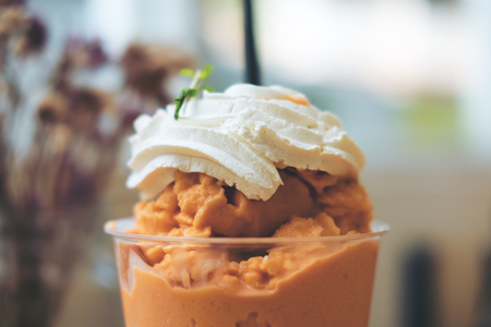 Close up image of Thai tea milk shake and whipped cream on the top in a glass with blue flower backgroundの写真素材