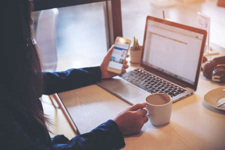 A business woman holding coffee cup and using smart phone and laptop in office