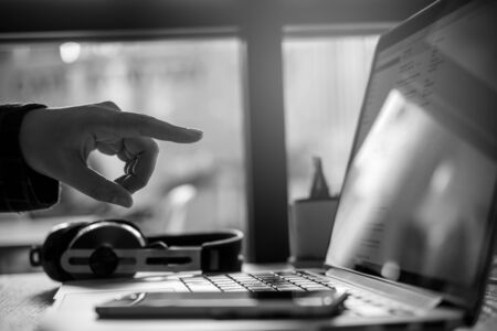 Black and white image of a business woman pointing her fingers at laptop in office with smart phone...