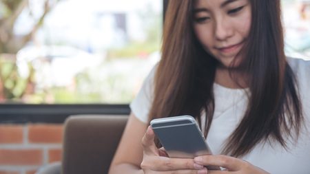 A beautiful Asian girl with smiley face holding and using smart phone in coffee shopの写真素材