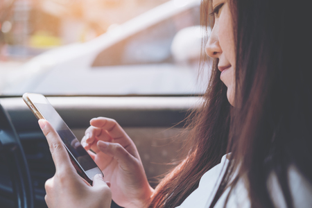 An Asian woman using and looking at smart phone in a car on the roadの写真素材