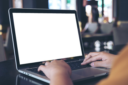 Mockup image of a woman using laptop with blank white screen on wooden table in modern cafeの写真素材
