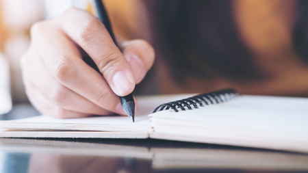Close up image of woman's hand writing on notebook with wooden table backgroundの写真素材
