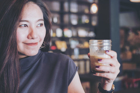 Closeup image of  a beautiful Asian woman holding and drinking hot coffee with feeling good in modern loft cafeの写真素材