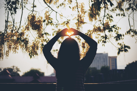 Silhouette image of a woman making heart hand sign with nature backgroundの写真素材