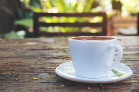 A white cup of hot coffee on vintage wooden table with blur green nature backgroundの写真素材