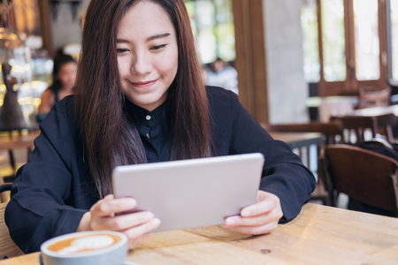 A beautiful Asian woman with smiley face using tablet in modern cafeの写真素材