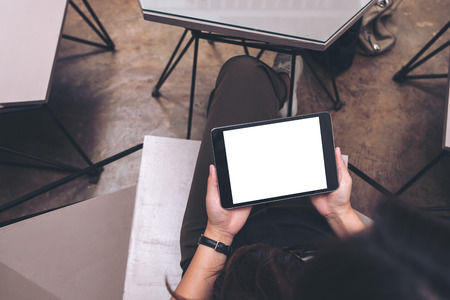 Top view mockup image of a woman holding black tablet pc with blank white screen in modern cafeの写真素材