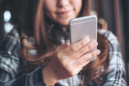 Closeup image of a beautiful Asian woman holding , using and looking at smart phone in modern cafeの写真素材
