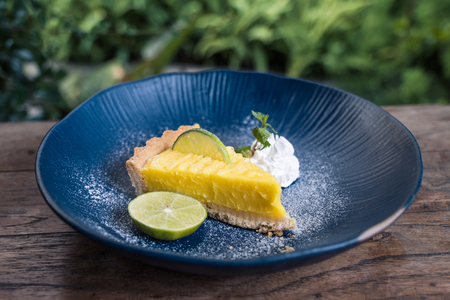 Closeup image of a yellow lemon curd cake in blue ceramic plate on wooden table with green nature backgroundの写真素材