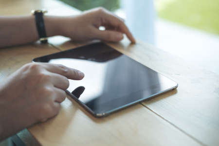 Closeup image of a woman's hands pointing , touching and using tablet pc  on wooden table in cafeの写真素材