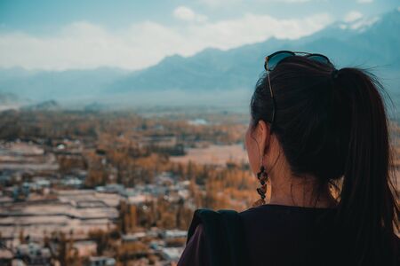 Portrait image of a beautiful Asian woman sitting , turn back and looking at a city , mountains , blue sky and green nature backgroundの写真素材