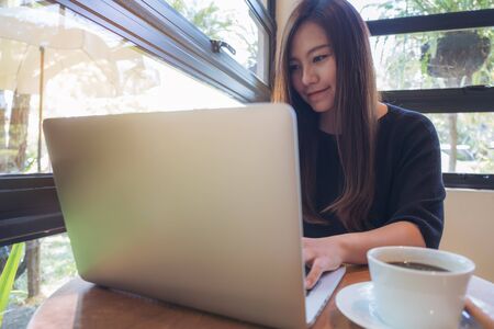Closeup image of a beautiful Asian business woman working and typing on laptop keyboard with coffee cup on wooden tableの写真素材