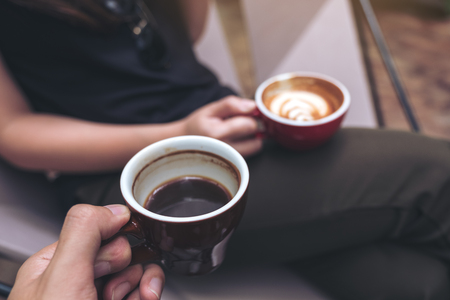 Closeup image of two people sitting and holding coffee cups in modern cafeの写真素材